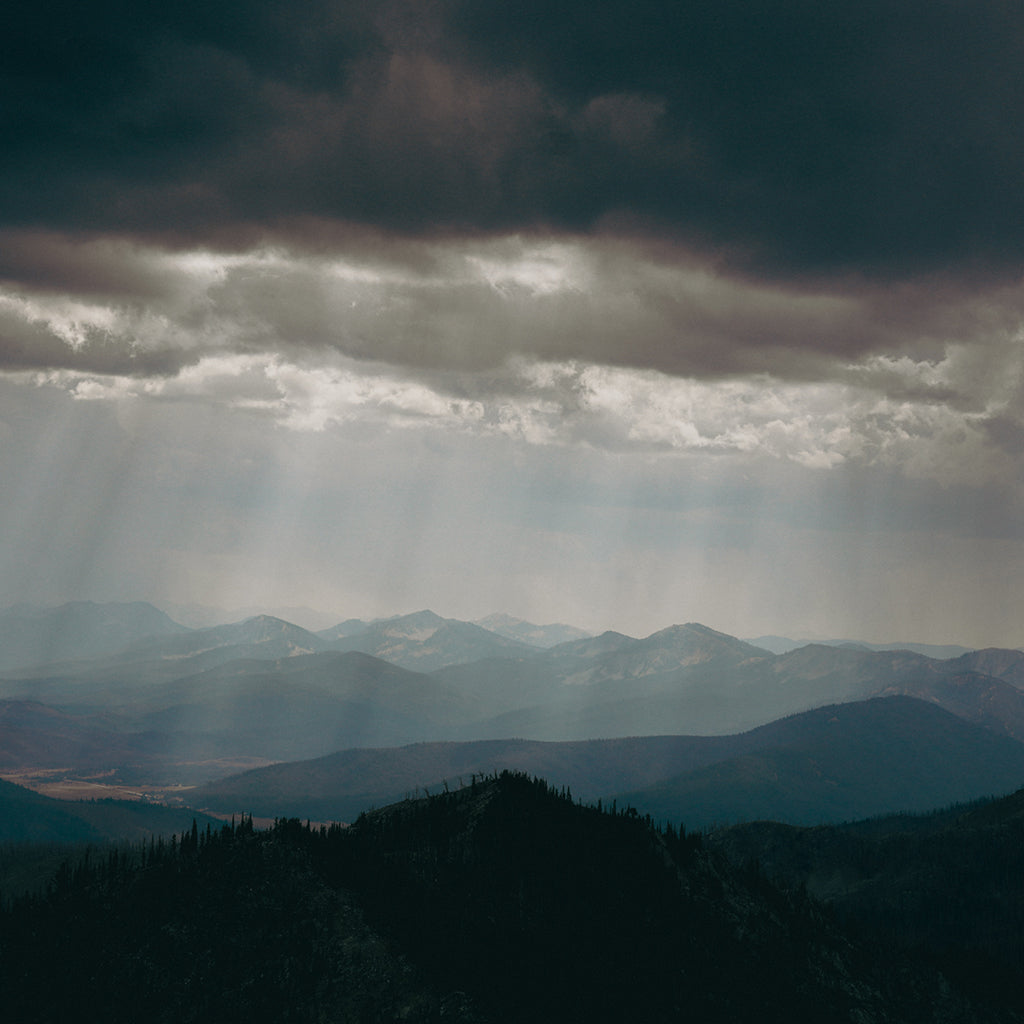 Sun rays piercing through dark clouds over a mountain landscape
